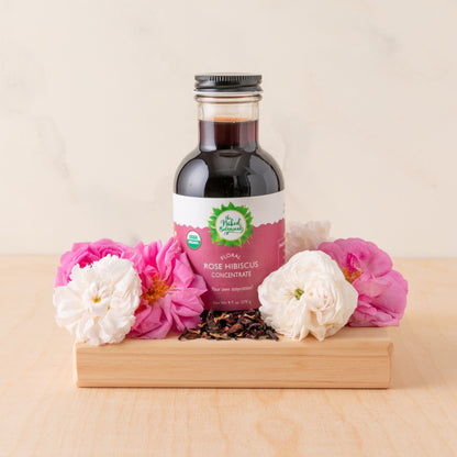 Bottle of  Rose Hibiscus Concentrate with flowers on a wooden stand
